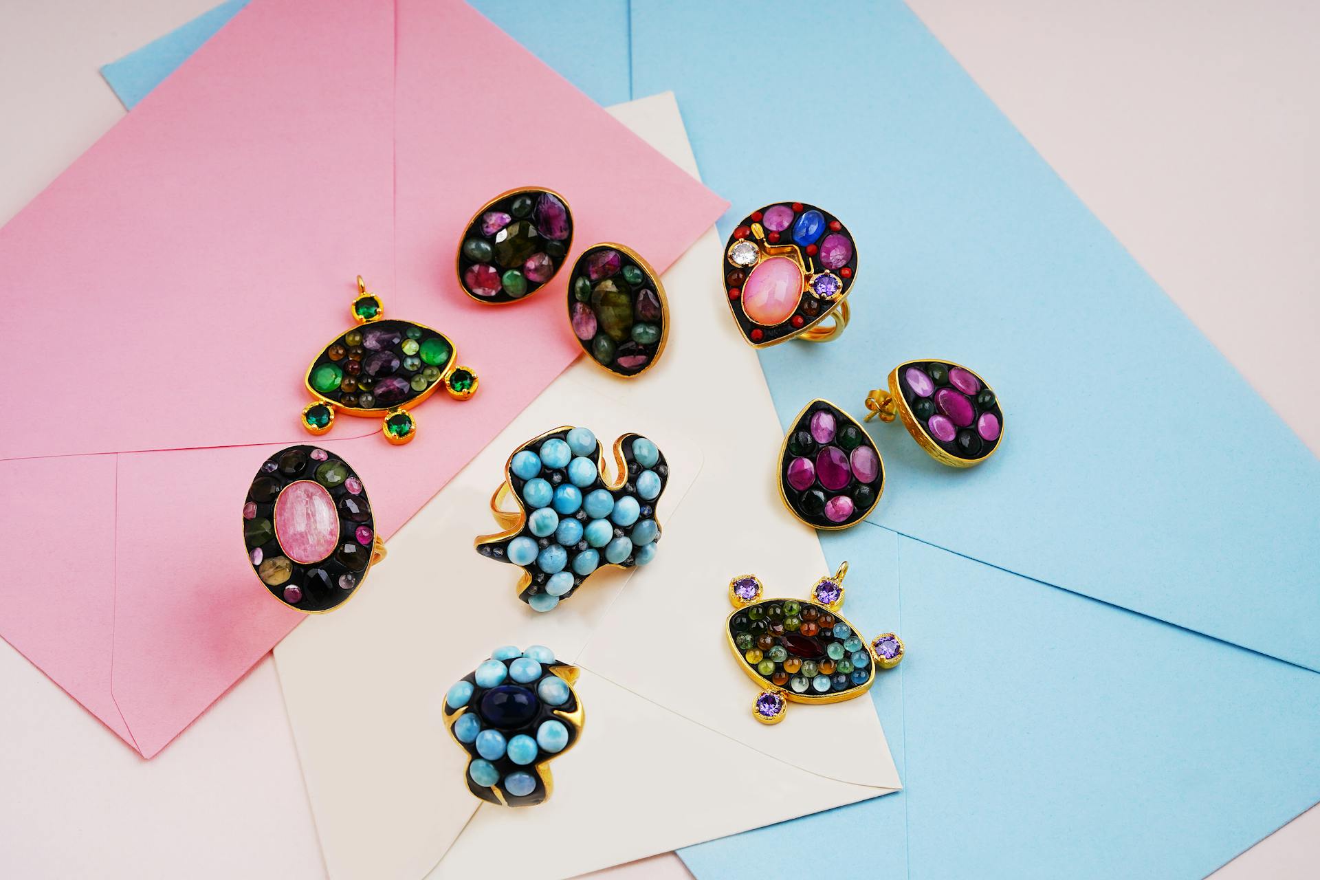 Vibrant gemstone jewelry pieces arranged on pastel pink and blue envelopes, showcasing elegance and color.