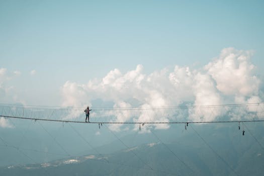 A man courageously walks across a rope bridge high above Sochi's scenic landscape.