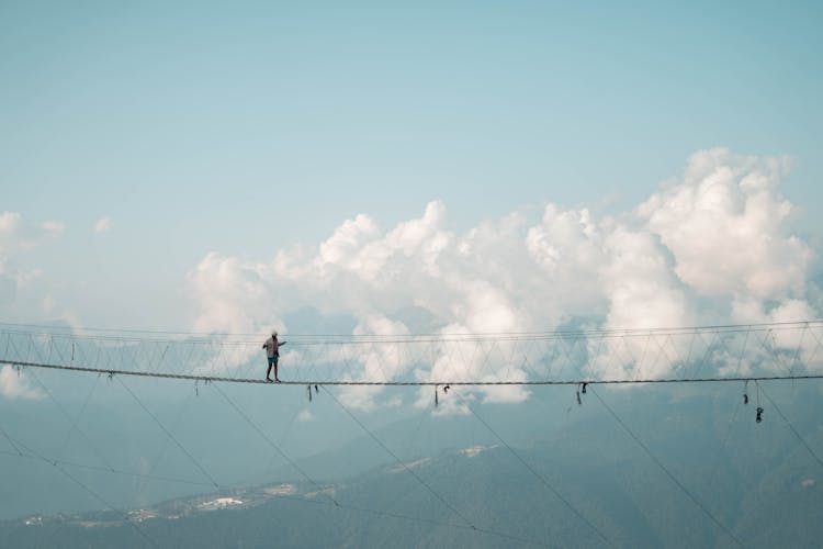 Man Walking On Rope Bridge Over Precipice