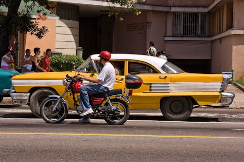 Yellow Car beside a Man riding a Motorcycle 