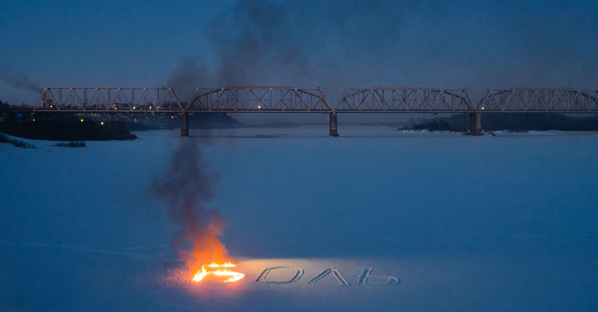 Aerial night view of a snowy river in Moscow with burning text and a steel bridge.