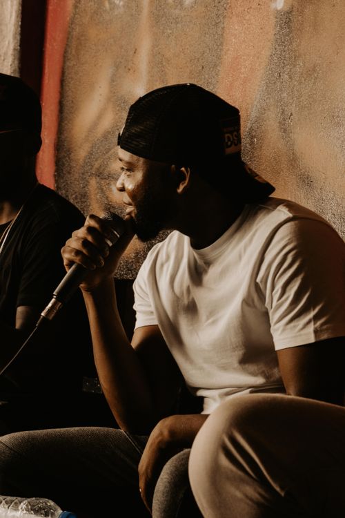 Free Black man in cap holding microphone in casual setting, singing or rapping. Stock Photo