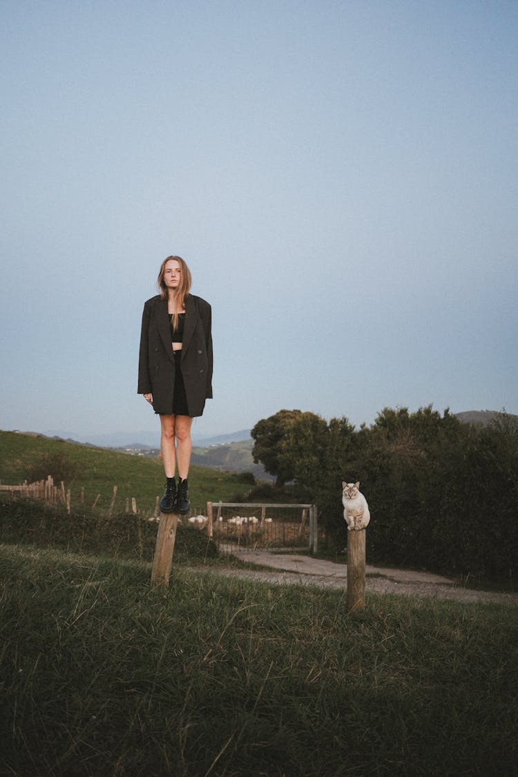 Woman Standing On A Stake And Cat Sitting On A Stake Next To Her