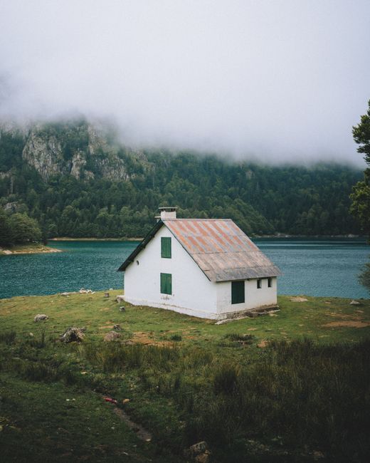Charming white house near a misty lake surrounded by forest and mountains.