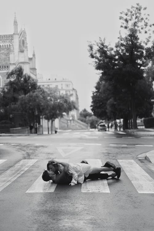 Free Couple Kissing while Lying on Zebra Crossing on Street in Black and White Stock Photo