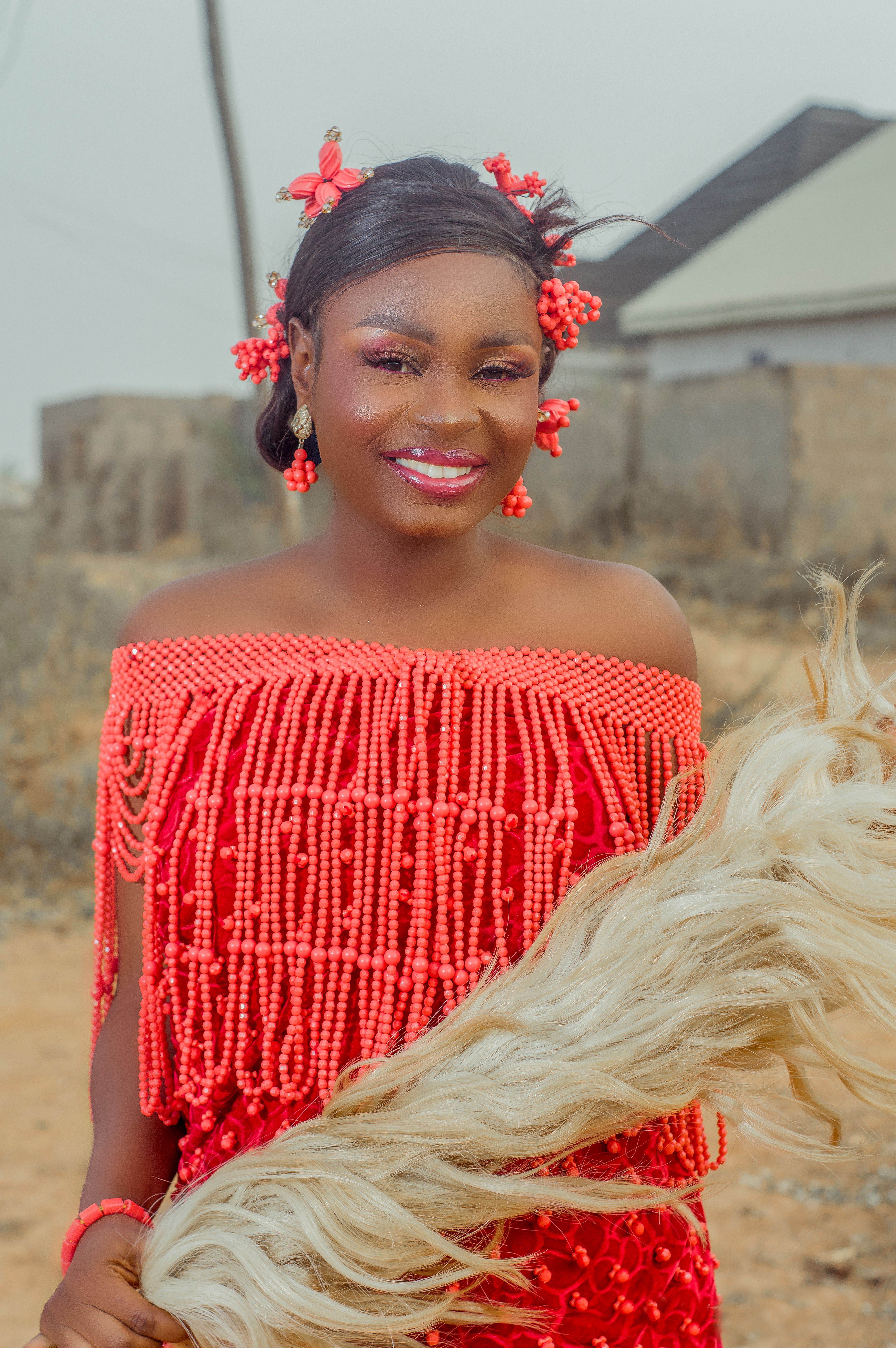 Smiling bride in vibrant Nigerian traditional wear holding a horsehair whisk.