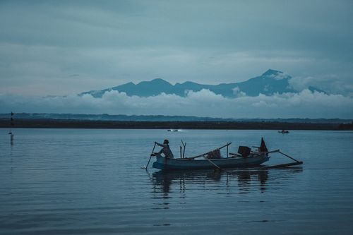 Free A lone fisherman in a traditional boat on the calm waters of West Nusa Tenggara, Indonesia, with mountains in the background. Stock Photo