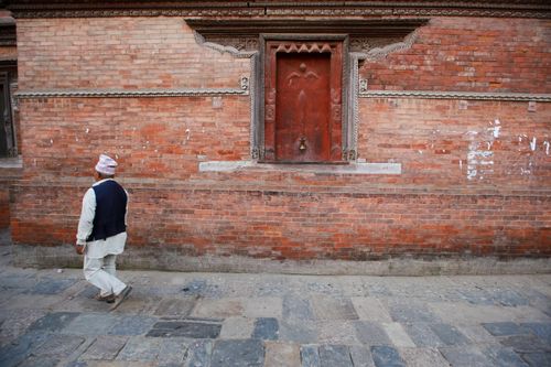 Free Man in traditional attire walks past an old brick wall with detailed carvings. Stock Photo
