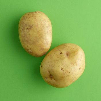 Two fresh potatoes on a vibrant green background, perfect for food-related themes.