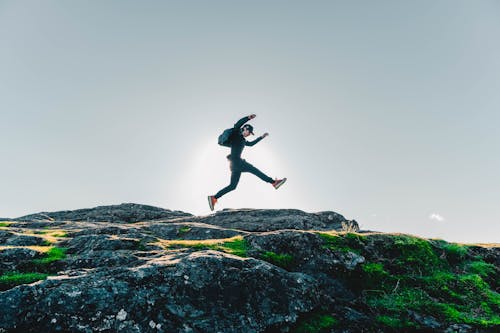 Free Man in Black Jacket and Pants Jumping on Rocky Mountain Stock Photo