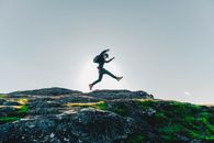 Man in Black Jacket and Pants Jumping on Rocky Mountain