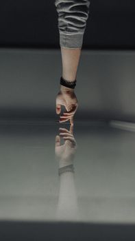 A hand reaching towards its reflection on a glass surface, creating a symmetrical effect.
