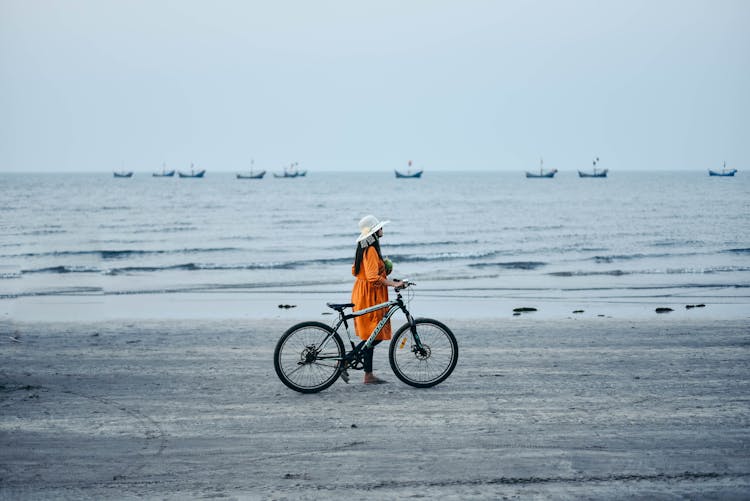 Woman In Orange Dress Holding A Bike While Walking At The Beach