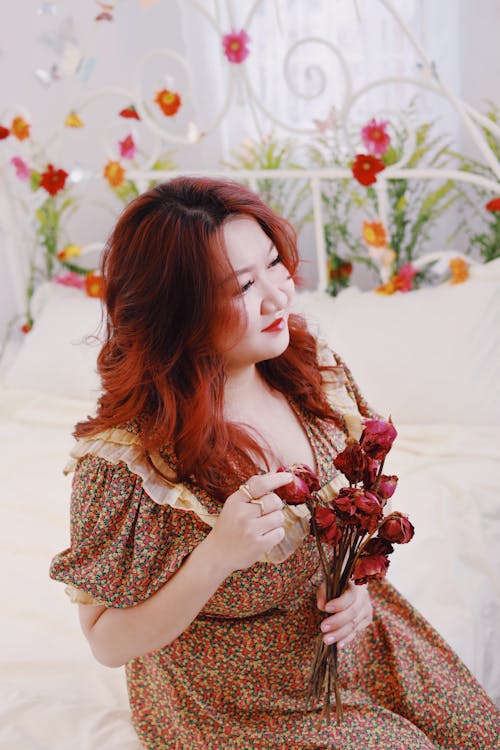 Free Woman in Brown and White Floral Dress Holding Red Flowers Stock Photo