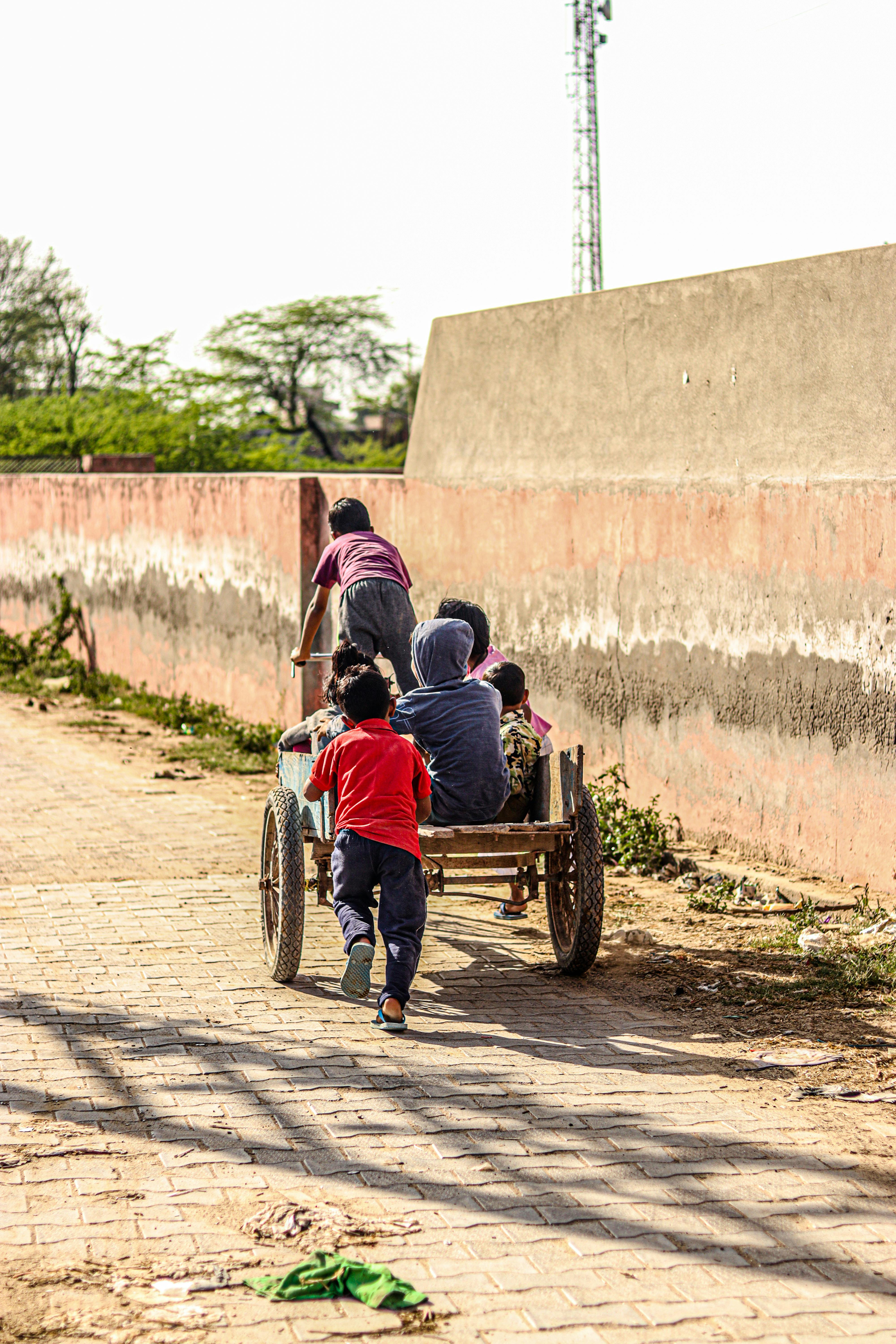 Group of children joyfully playing on a cart in a rural village street, back view.