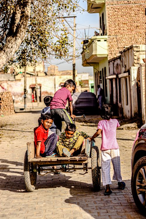 Free Group of boys enjoying a playful ride on a rustic cart in a vibrant town street. Stock Photo