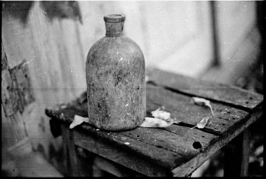 Monochrome photo of an old bottle on a wooden table, capturing rustic charm.