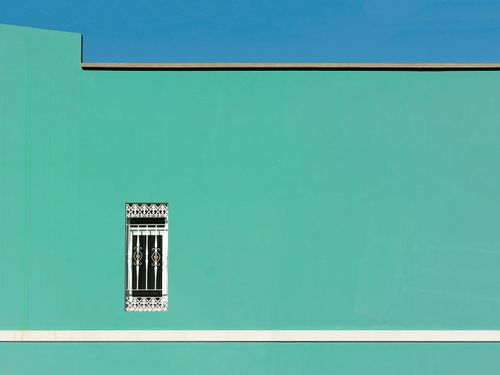 Free A vibrant minimalist green wall featuring an ornate window against a clear blue sky. Stock Photo
