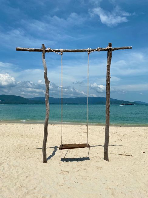 Wooden swing on a sandy beach with clear ocean and blue sky, perfect for relaxation.