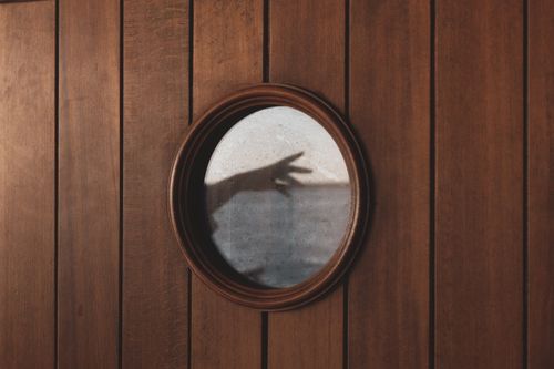 Free Artistic shadow hand reflection in round mirror on wooden wall creates intriguing visual contrast. Stock Photo