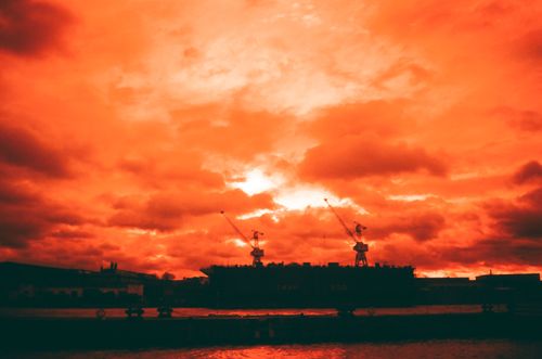Free A dramatic orange sunset with silhouetted cranes and clouds in a vivid sky. Stock Photo