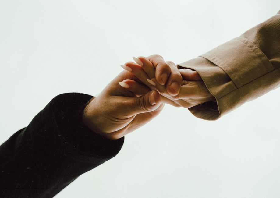 Intimate close-up of two hands clasped together against a white sky, symbolizing support.