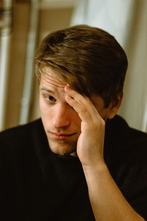 Free Close-up of a young man holding his head, expressing contemplation or stress indoors. Stock Photo