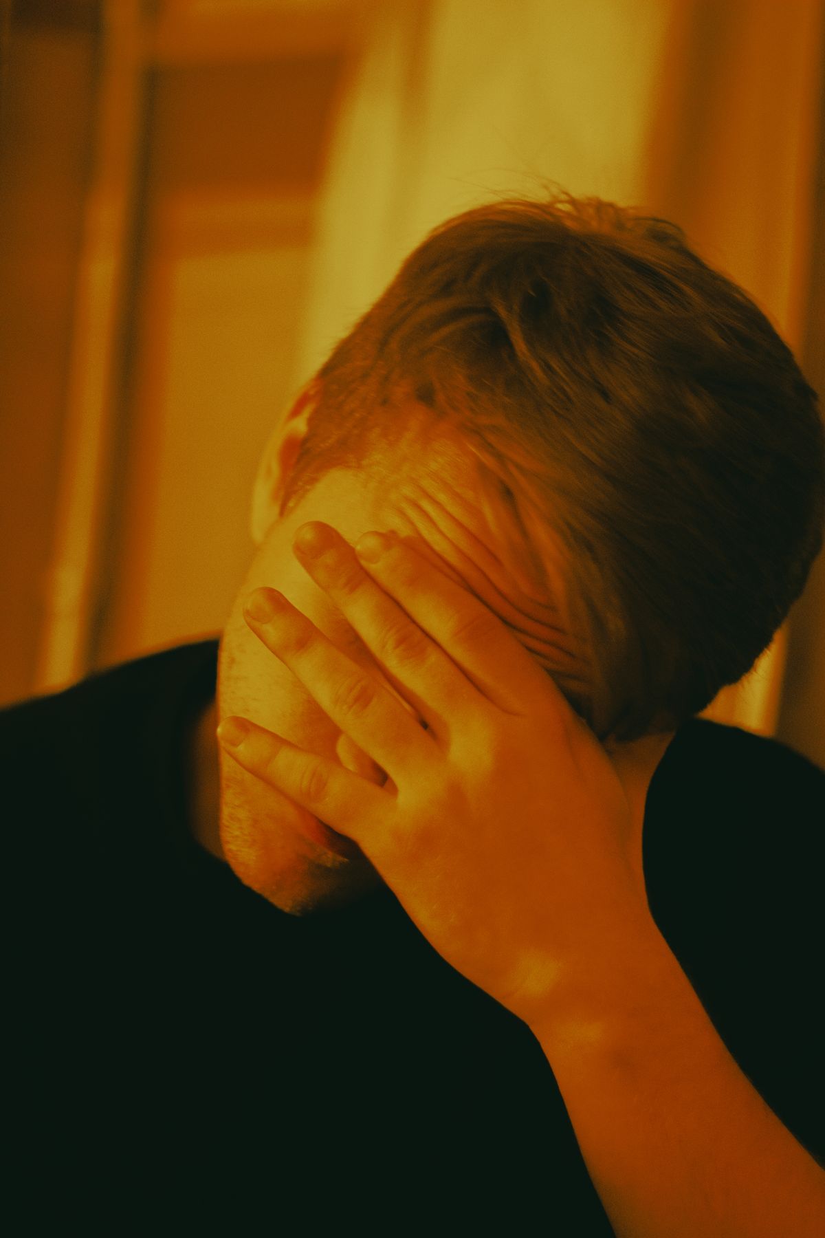 Person in a dark shirt covering their face with a hand
