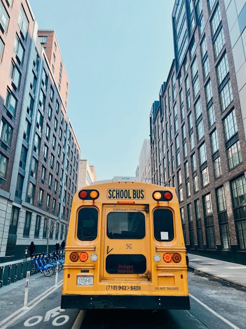 Free Yellow School Bus Parked Between Tall Buildings Stock Photo