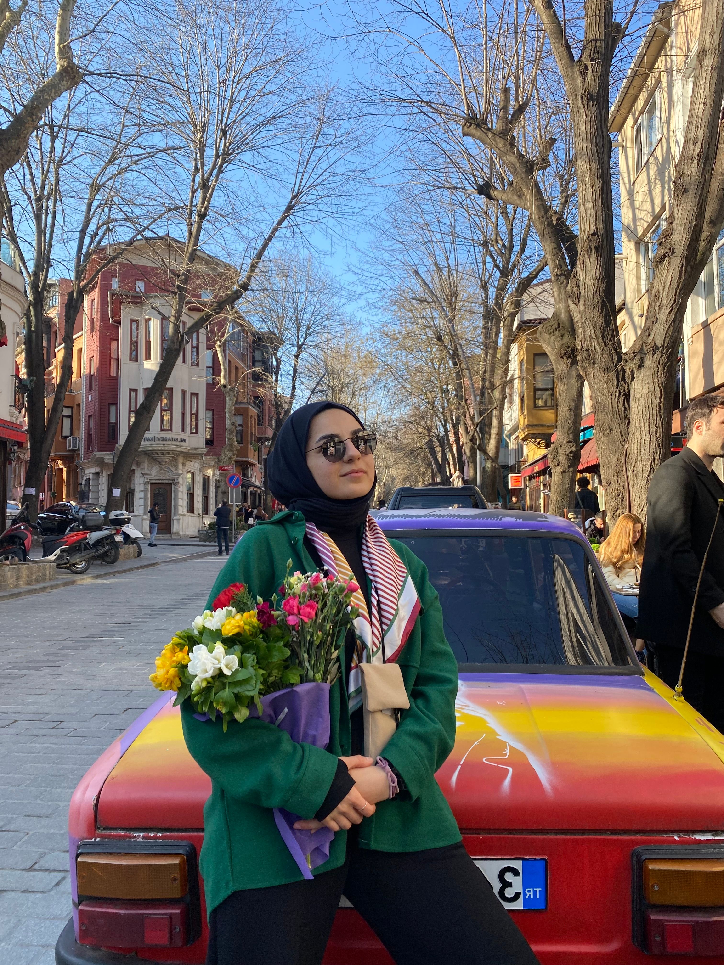 Woman in a vibrant street scene holding flowers next to a colorful car.