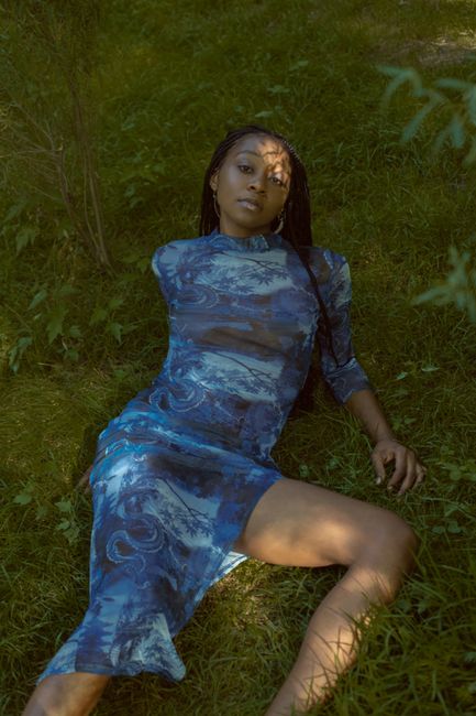 Portrait of a woman in a blue dress reclining on grass surrounded by nature.