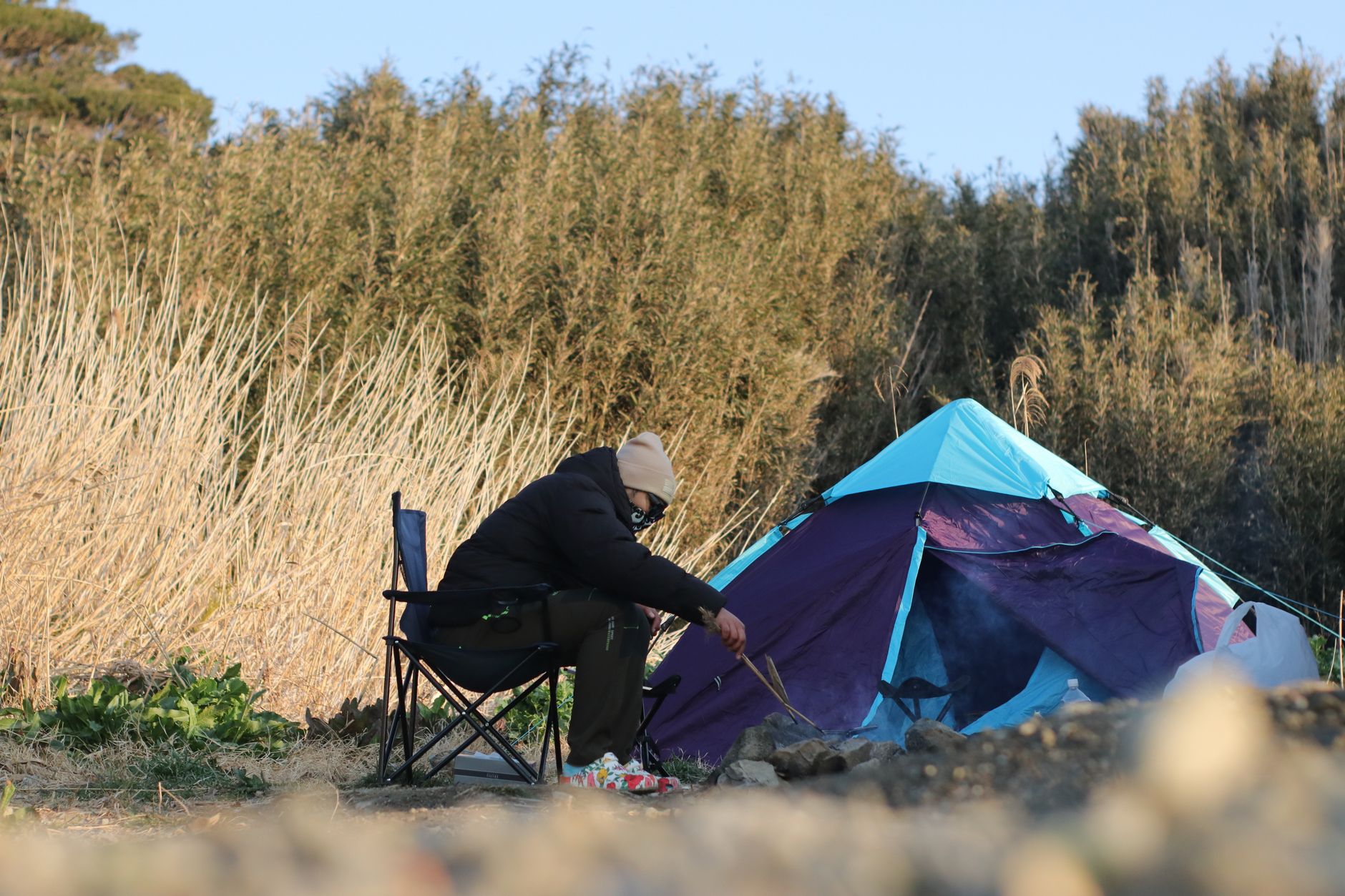 A person enjoys a peaceful camping scene with a colorful tent in the tranquil outdoors of Kanagawa, Japan.