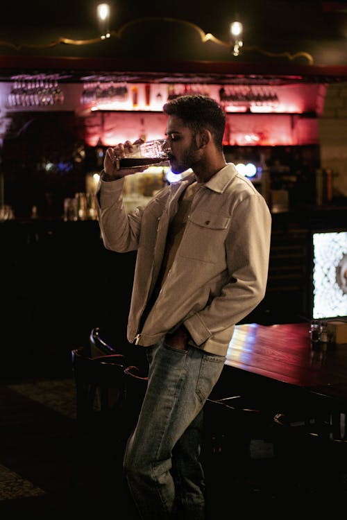 Man in White Jacket Drinking With Hand Inside the Pocket 