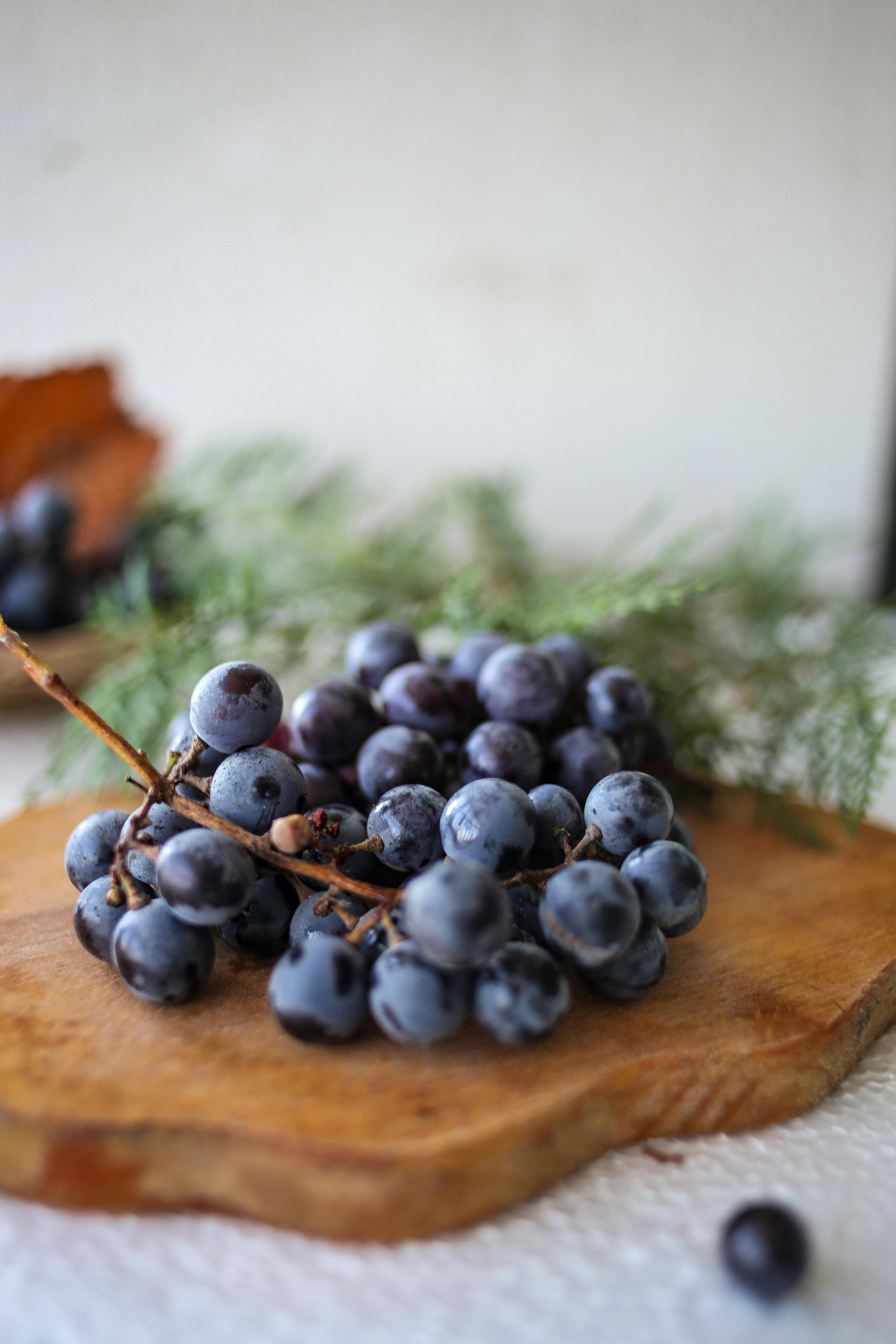 A bunch of fresh blue grapes on a wooden cutting board, perfect for still life photography.