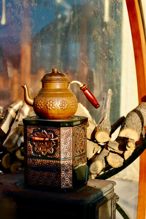 Free Antique brass teapot on decorative stove with firewood background. Ideal for vintage and rustic themes. Stock Photo