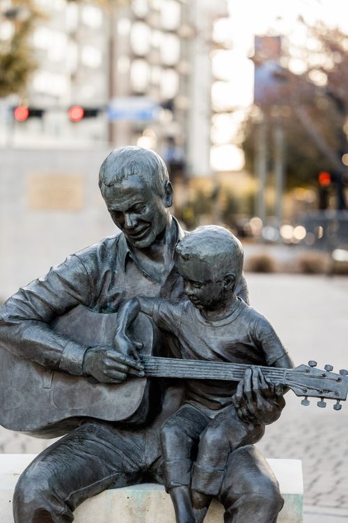 Free Bronze statue of a father and child playing guitar, symbolizing music and togetherness. Stock Photo