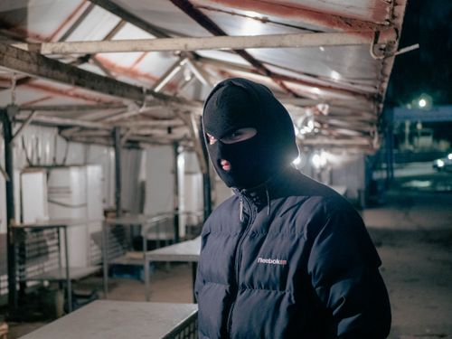Free A person in a balaclava and jacket standing at an empty night market, creating a mysterious mood. Stock Photo
