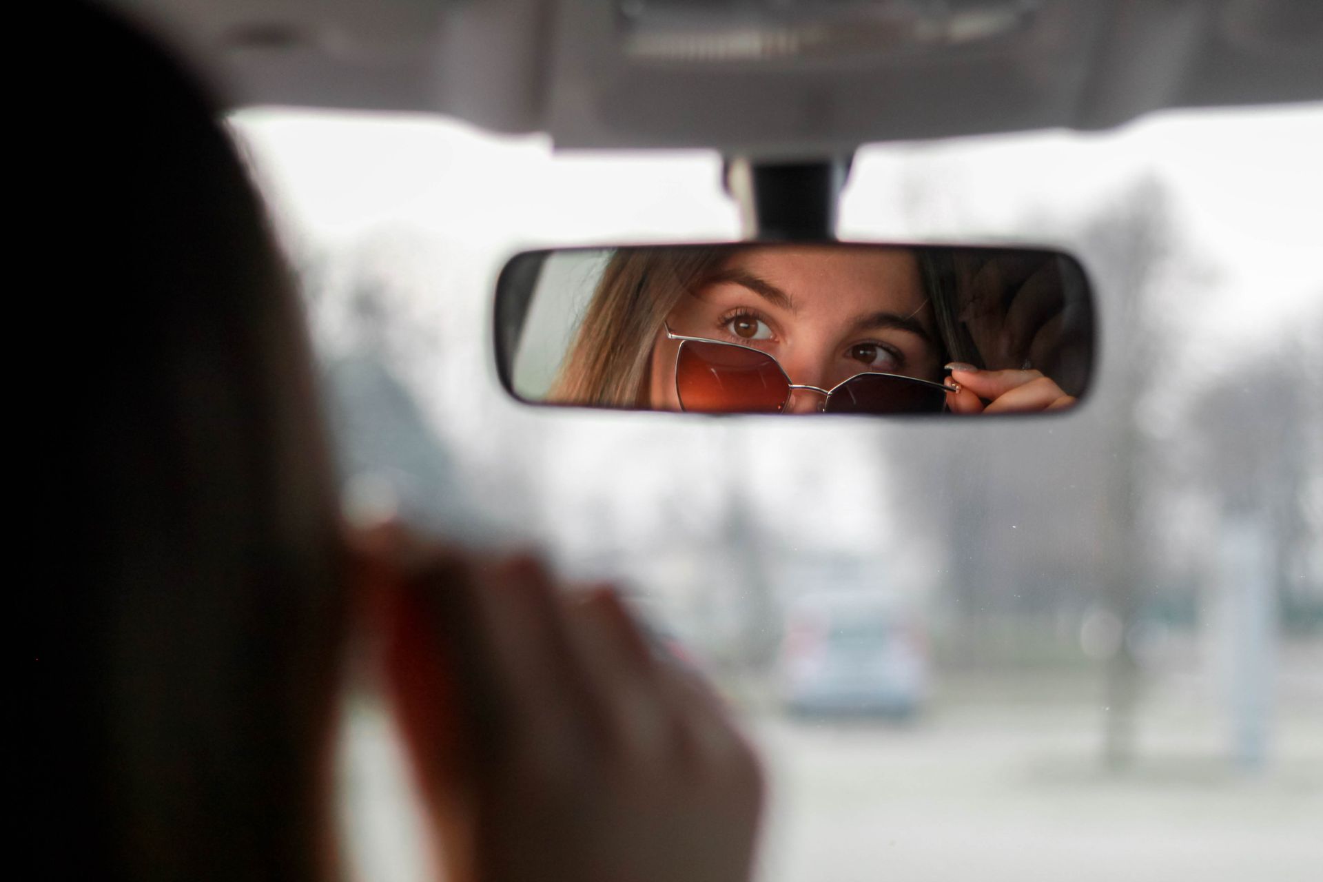 Woman in car adjusts sunglasses in rearview mirror, capturing a private reflective moment.