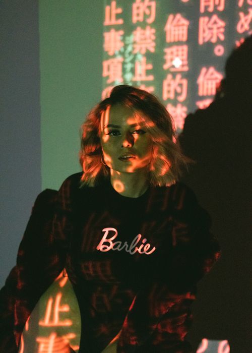 Free A woman in black attire poses in a studio with colorful text projections. Stock Photo