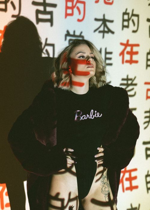 Free A stylish woman stands against a wall with kanji projections, showcasing bold fashion. Stock Photo