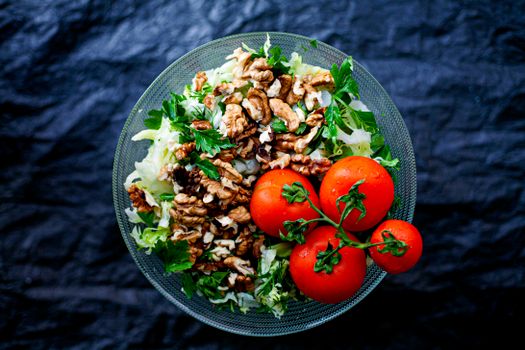 Top view of a fresh mixed salad with walnuts and tomatoes in a glass bowl, emphasizing healthy eating.