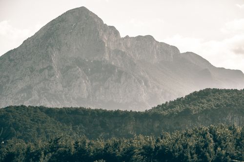 Free Beautiful view of a towering mountain enveloped by mist, with lush green forest at its base. Stock Photo