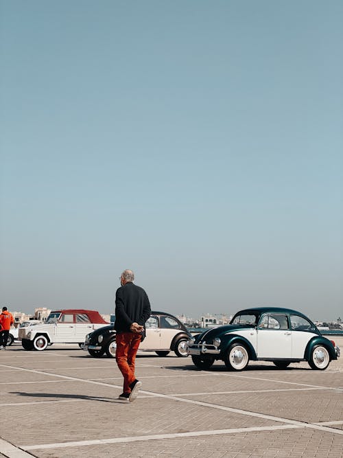An Elderly Man Walking on a Parking Lot with Parked Volkswagen Cars