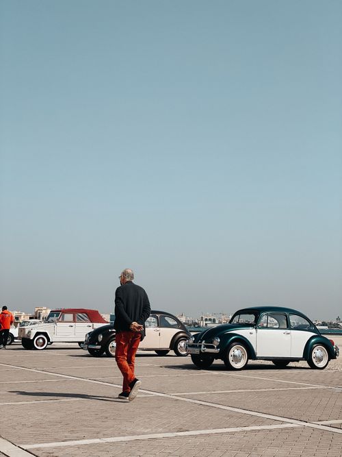 Free An elderly man walks among classic vintage cars parked under a blue sky. Stock Photo