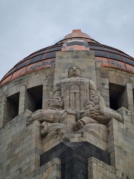 Low angle view of the iconic Monument to the Revolution with sculptures on a cloudy day.
