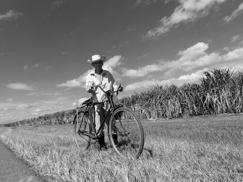 Grayscale Photo of Man Pushing his Bicycle in the Grass Field