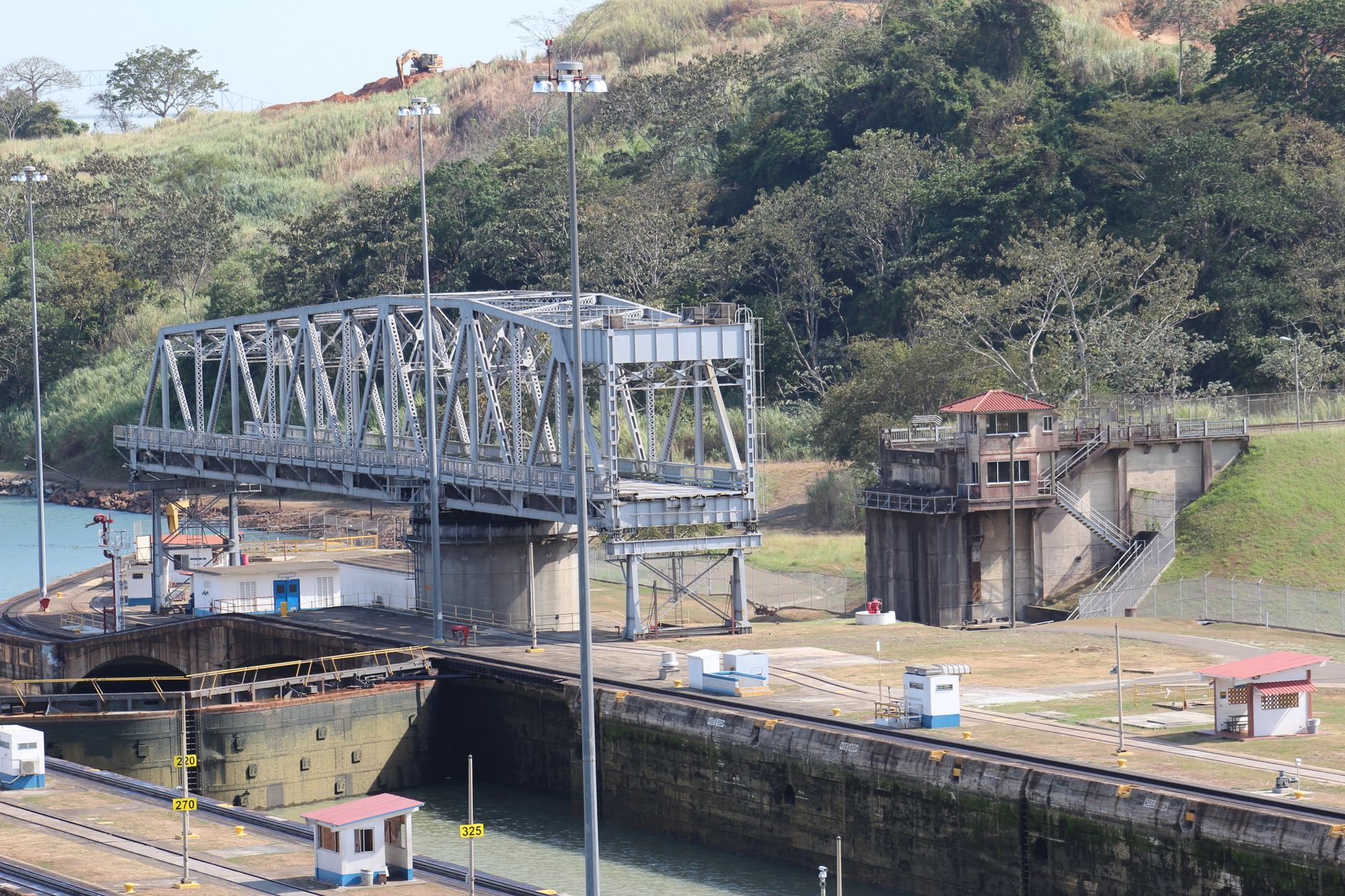Steel bridge spanning a canal lock amidst lush greenery, captured from a high angle.