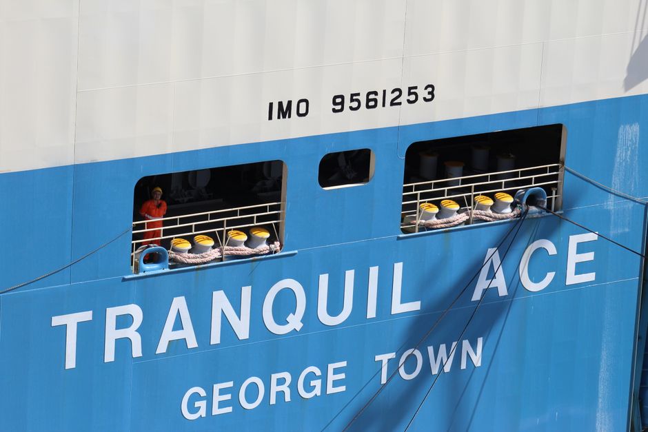 A worker in orange overalls on the Tranquil Ace ship docked in George Town port, offering a nautical scene.