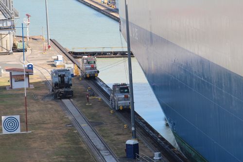 Free A large ship navigates through a canal with industrial machinery guiding its path. Stock Photo