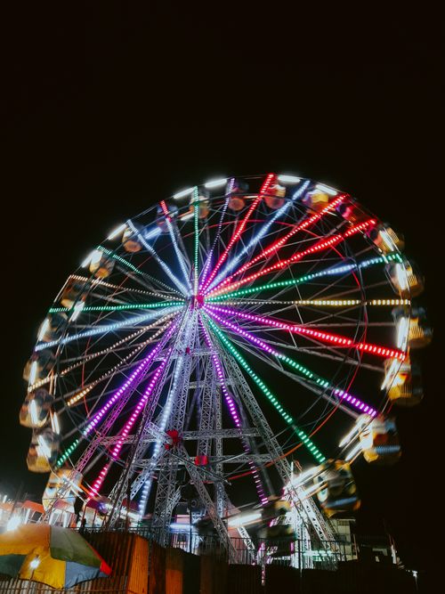 Free Vibrant Ferris wheel spins with multicolored lights against a dark night sky. Stock Photo